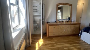 Een slaapkamer met houten vloer, een dressoir, een spiegel en een raam met gordijnen.