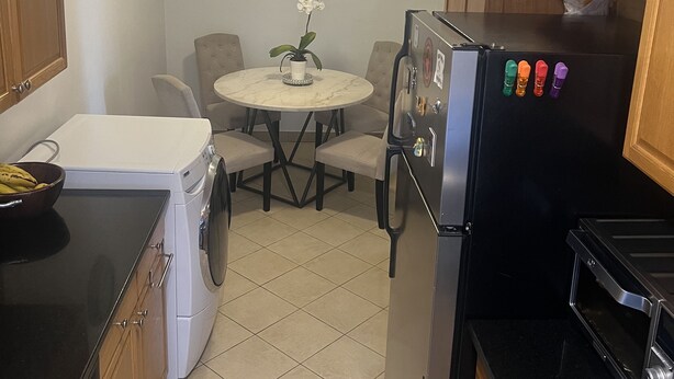 Een kleine keuken met een wasmachine, een koelkast, een kookplaat en een eettafel met stoelen.
