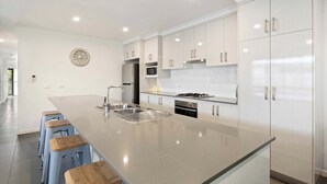 Une cuisine moderne dotée d’un grand îlot central, de tabourets de bar, d’appareils électroménagers en acier inoxydable et de meubles de cuisine blancs.