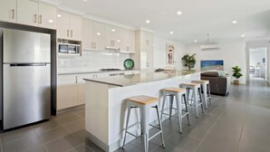 Une cuisine moderne avec des meubles blancs, des appareils en acier inoxydable et un îlot central doté de tabourets de bar.