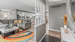 Ein modernes Wohnzimmer mit einem grauen Sofa, einem farbenfrohen Teppich und einem weißen Konsolentisch mit Dekoration.