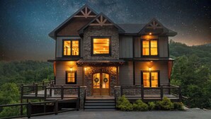 Ein zweistöckiges Haus mit einer Steinfassade, zahlreichen Fenstern und einer Veranda mit Stufen zum Eingang.