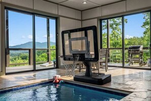 Un espace piscine équipé d’un panier de basket, de grandes fenêtres et offrant une vue sur la verdure.