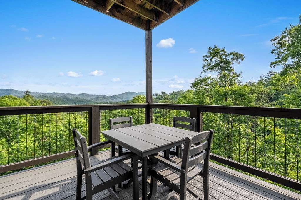 A wooden deck with a table and chairs, overlooking a forested landscape.