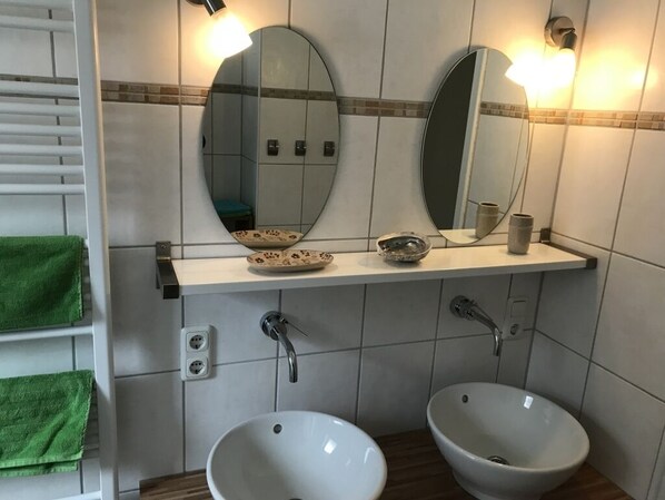 A bathroom with two sinks, a mirror, and a shelf with toiletries.