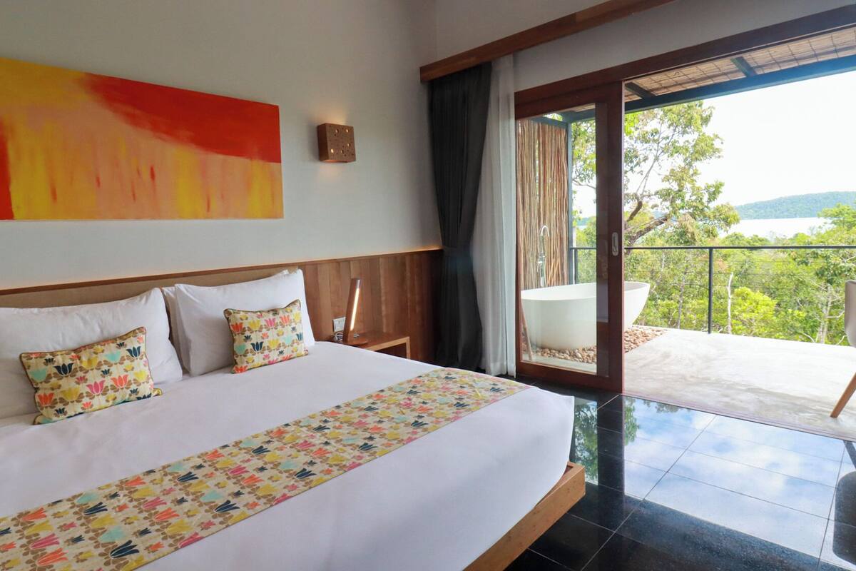 A hotel room with a large bed, a view of the outdoors, and a balcony with a chair.