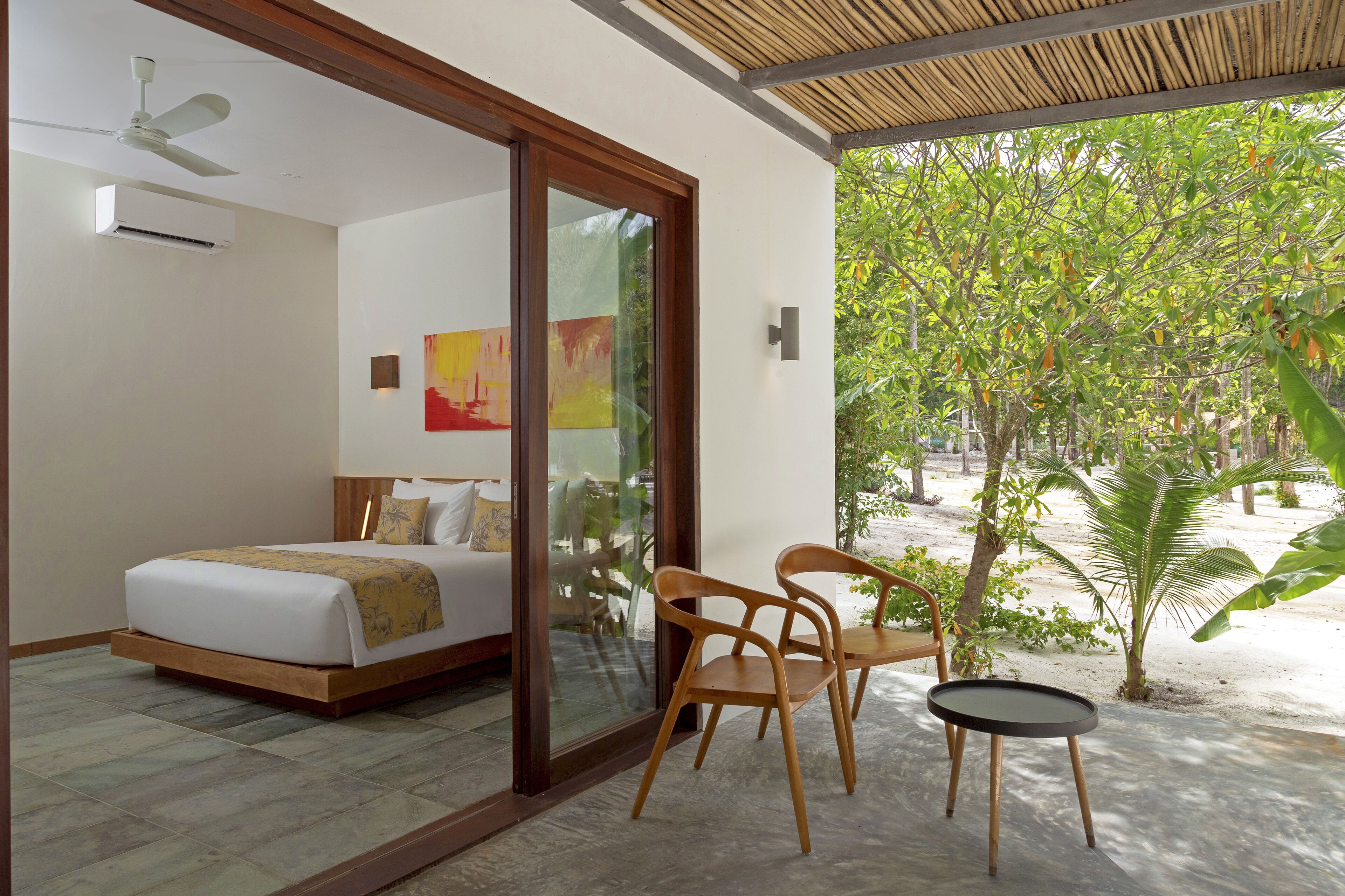 A bedroom with a bed, a ceiling fan, and a view of a tropical garden.