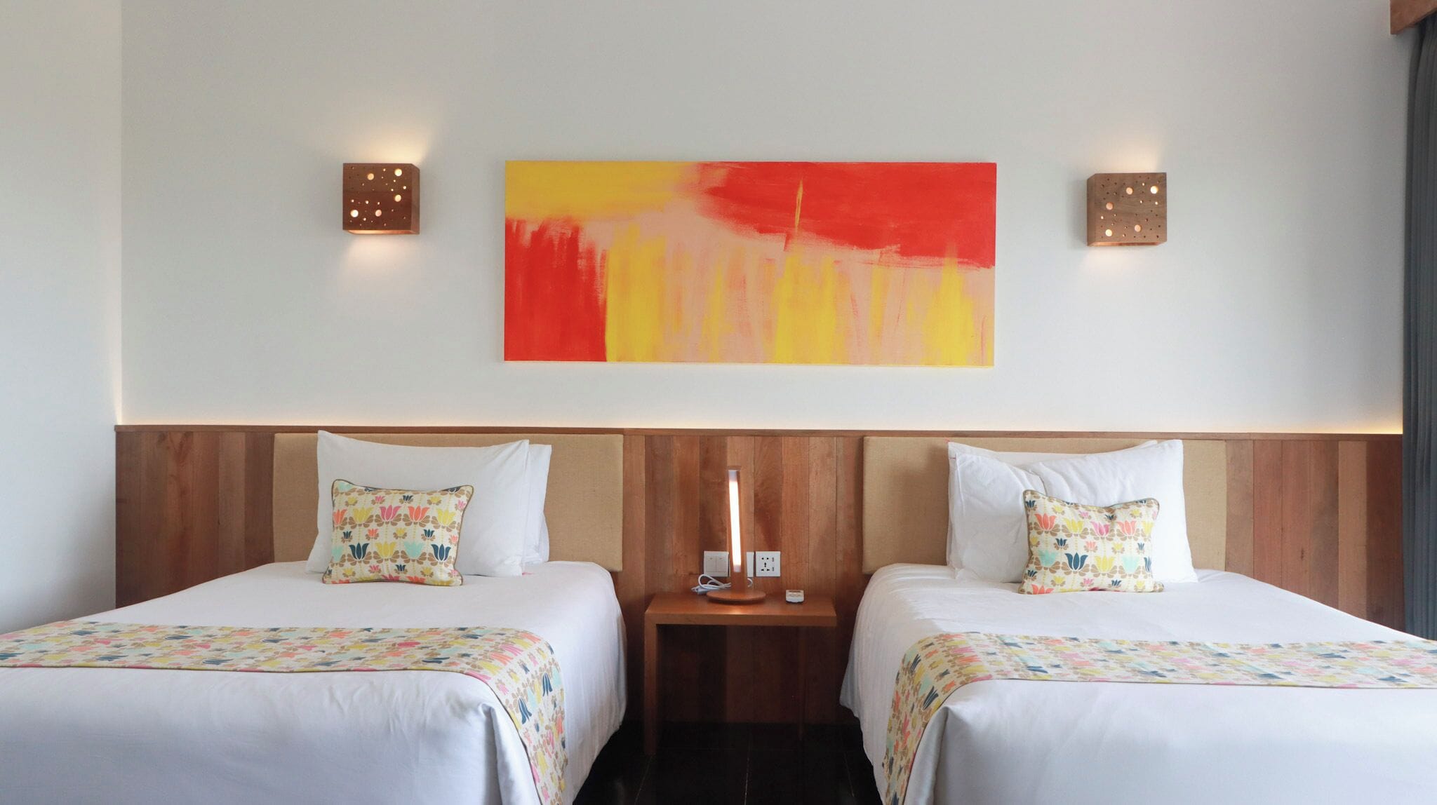 A hotel room with two beds, a wooden headboard, a nightstand, and a large abstract painting on the wall.
