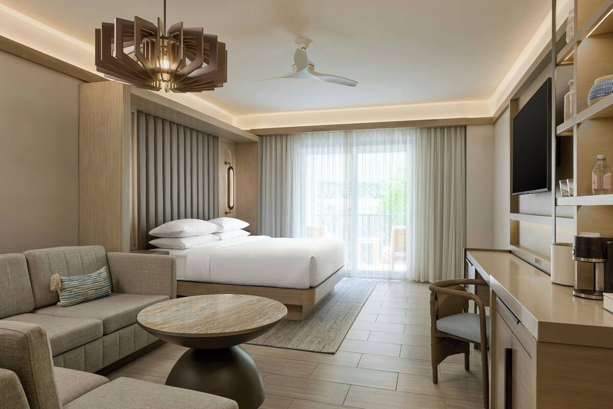 Una habitación de hotel moderna con cama, sofá, televisión y zona de comedor.