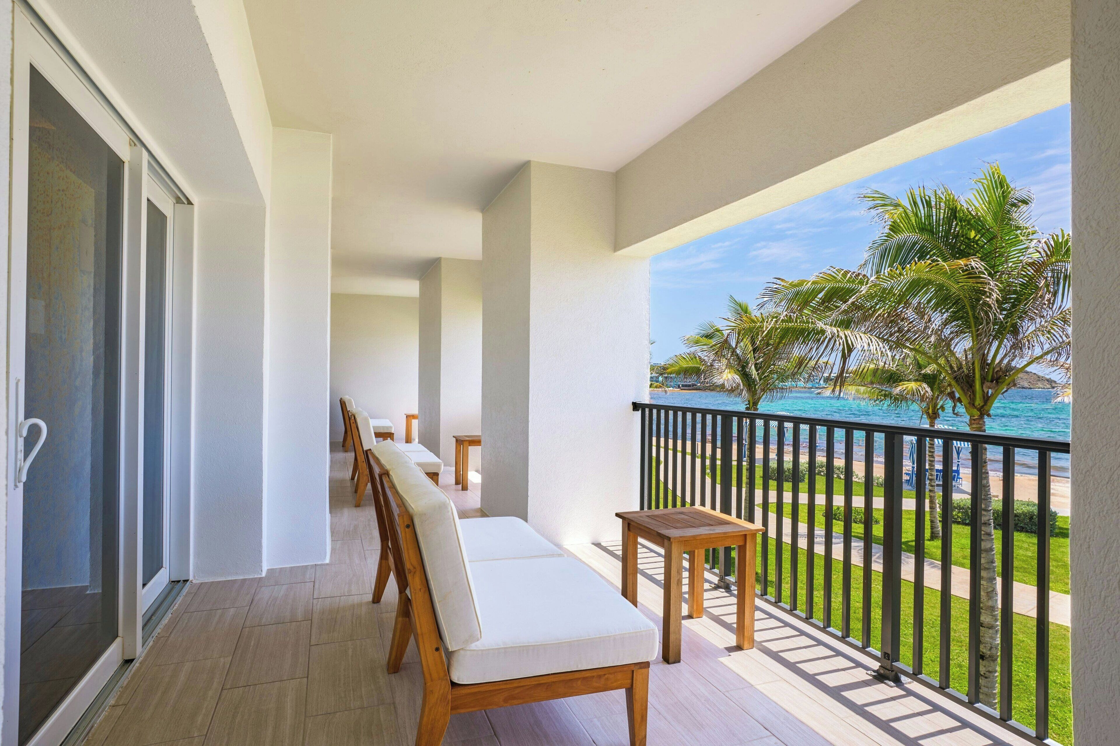 A balcony with a view of the ocean, a wooden bench, and a small table.