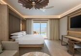 A modern hotel room with a large bed, a desk, a television, and a view of the ocean.