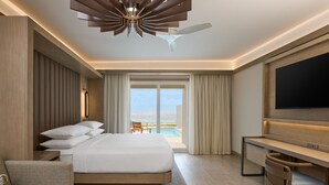 A modern hotel room with a large bed, a desk, a television, and a view of the ocean.