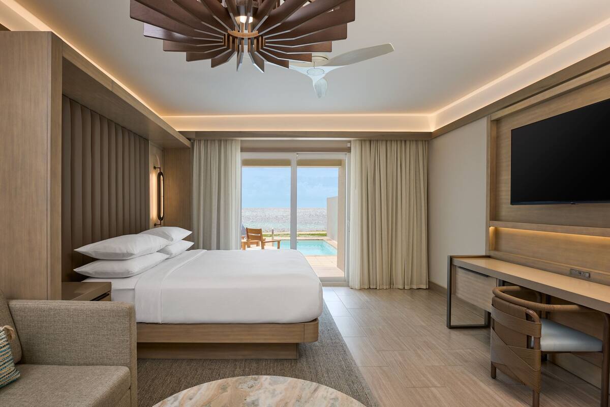 Habitación de hotel moderna con una cama grande, un escritorio, un televisor y vistas al océano.