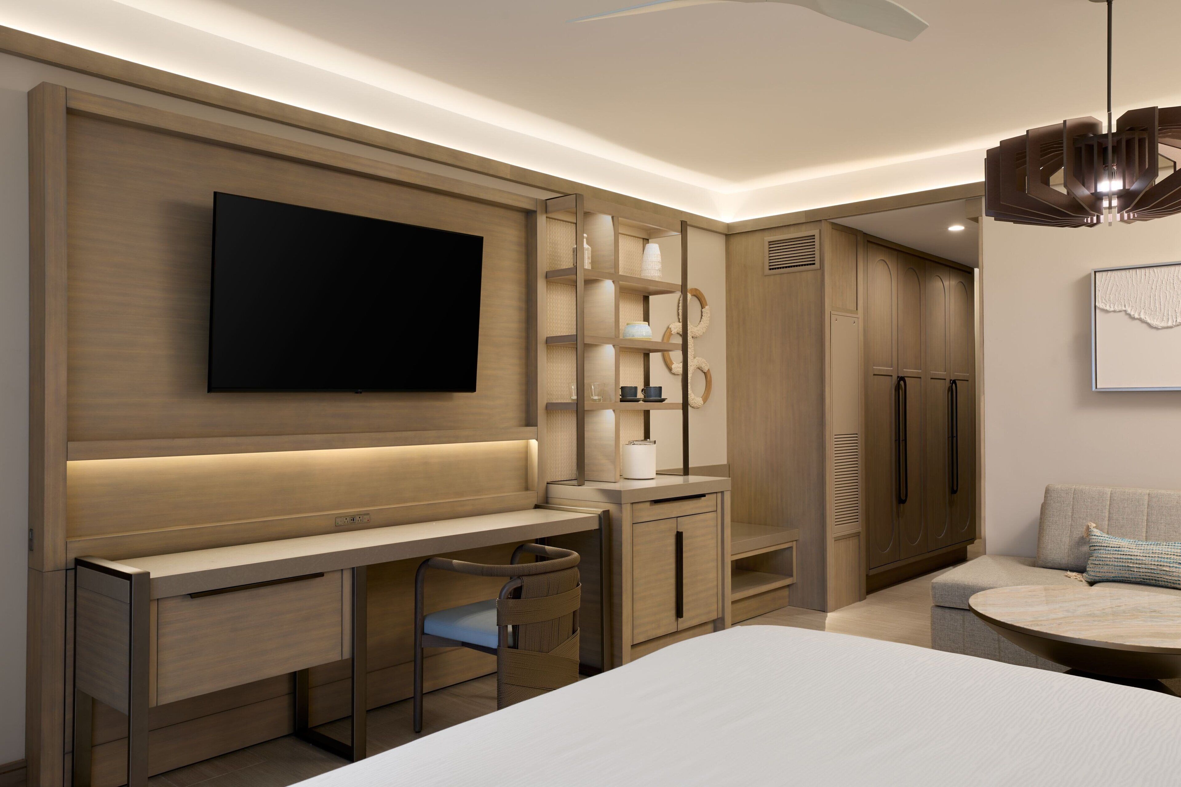 Une chambre d’hôtel moderne équipée d’une télévision à écran plat, d’un bureau avec une chaise, d’un canapé et d’une table basse ronde.