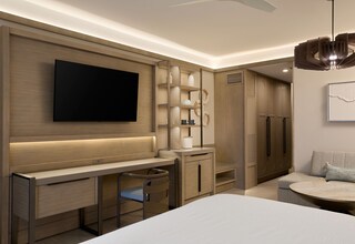 A modern hotel room with a flat-screen TV, a desk with a chair, a sofa, and a round coffee table.
