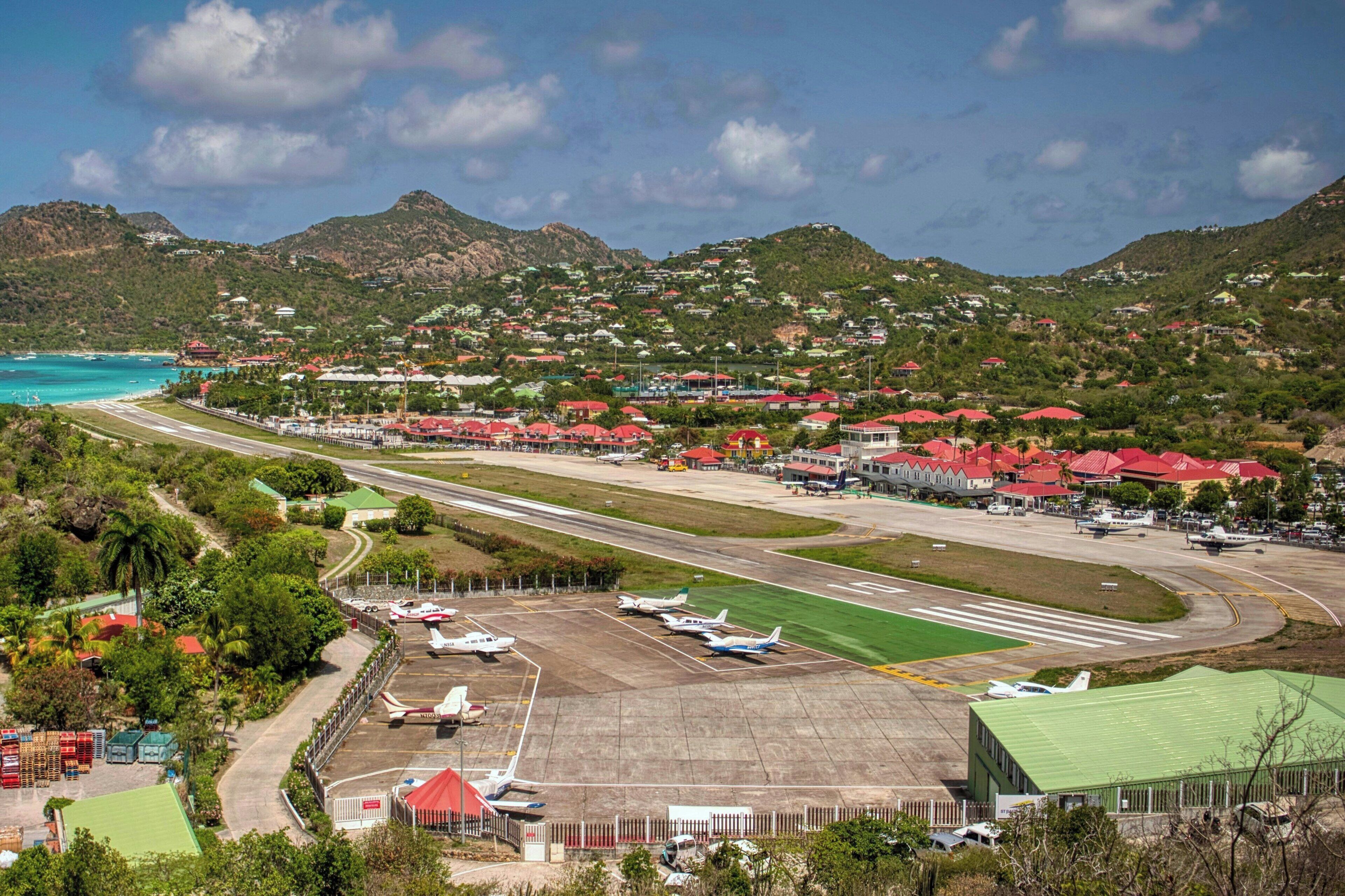 Um aeroporto com várias pistas, aeronaves estacionadas e edifícios com telhados vermelhos.