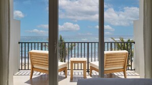 A balcony with two wooden chairs and a small table, overlooking a beach and ocean.