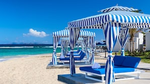 A beachside resort with striped blue and white umbrellas, lounge chairs, and a clear view of the ocean.