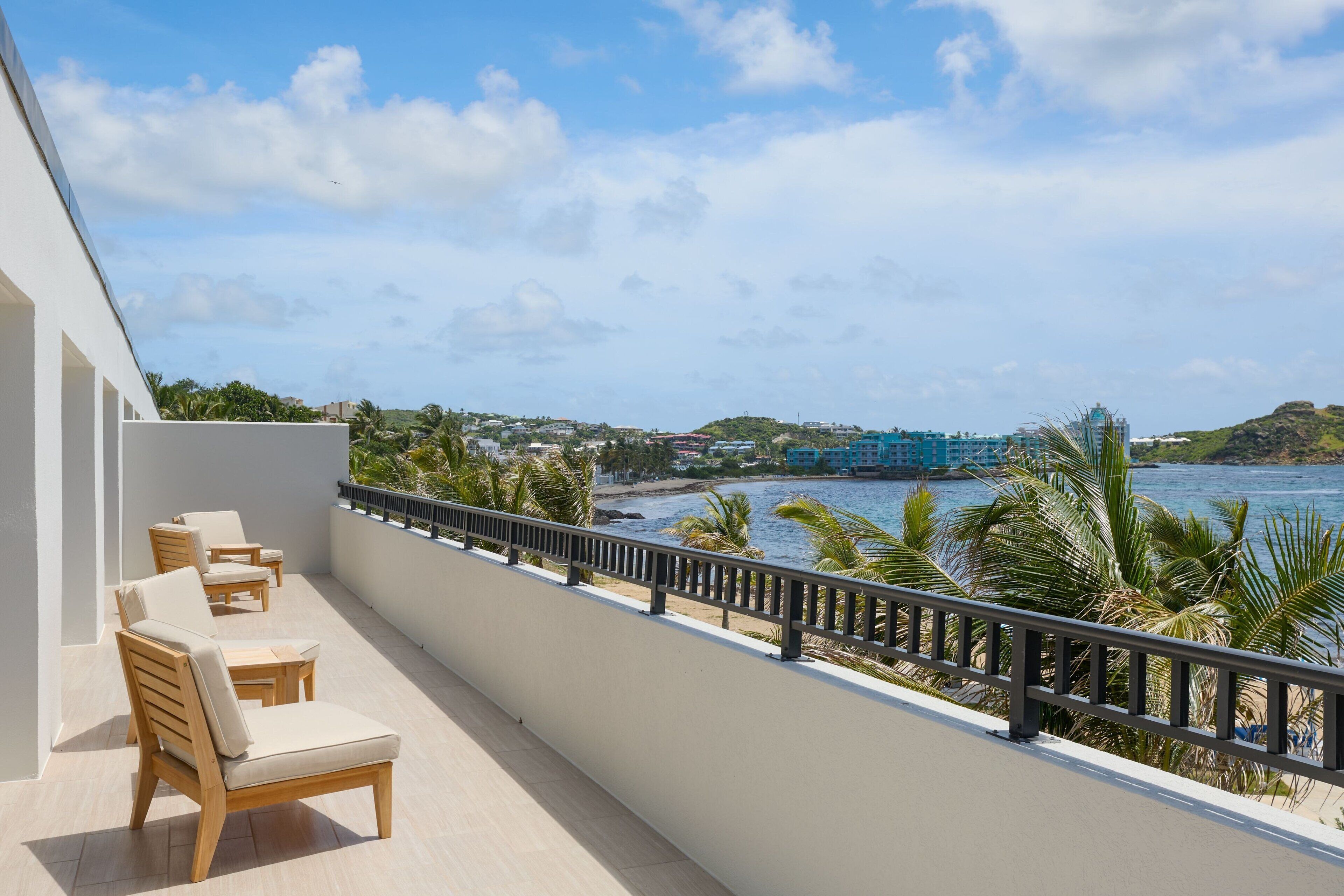 A balcony with wooden chairs and a view of a beach and water.