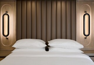 A neatly made bed with white linens and pillows, flanked by two wall sconces with a modern design.