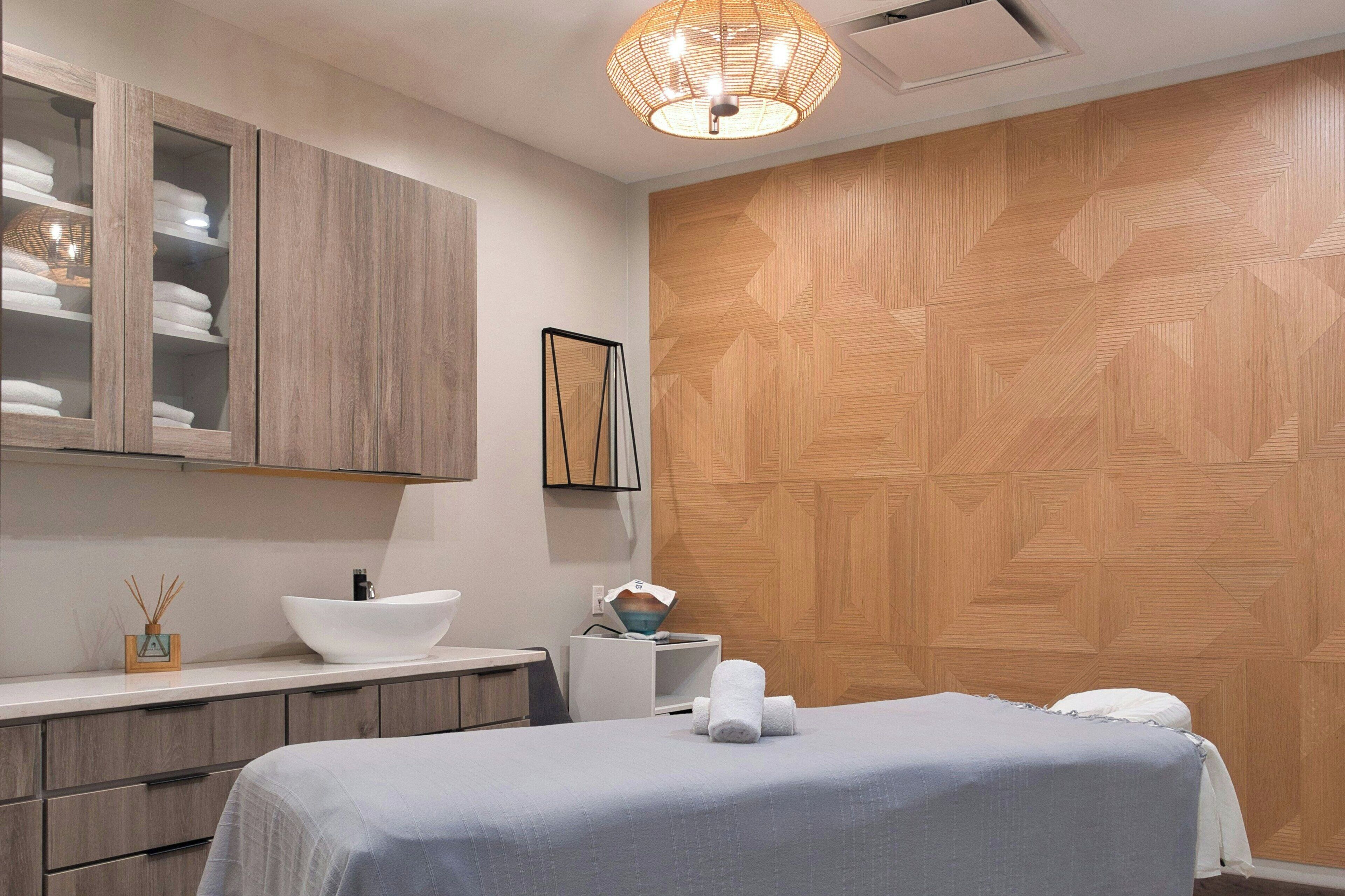 A modern bedroom with a bed, wooden wall paneling, a white bedside table, a white basin, and a hanging light fixture.