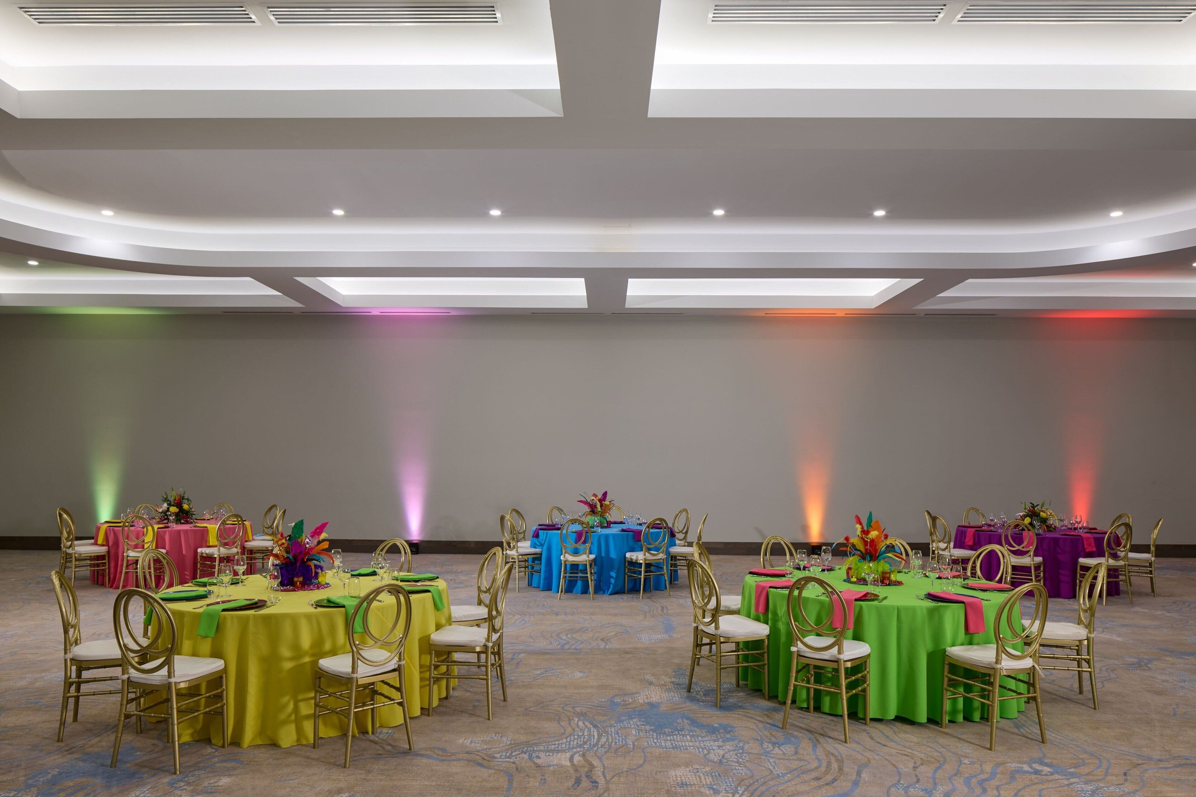 A conference room with round tables, gold chairs, and colorful tablecloths.