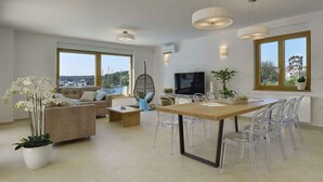 A modern living room with a sofa, coffee table, TV, and dining area with chairs.