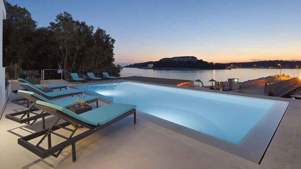 A swimming pool with lounge chairs, a view of the sea, and a distant island.