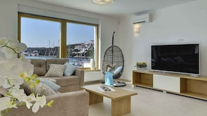 A modern living room with a sofa, a hanging chair, a coffee table, a TV, and a view of a marina.