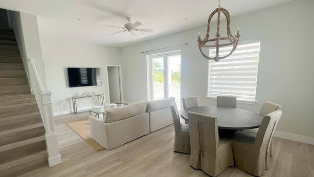 A spacious living area with a sofa, dining table, and chairs, a staircase, and a chandelier.