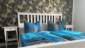 A bed with a white frame and blue bedding, flanked by two nightstands with lamps, against a textured wall. - Maja Ferienwohnung (Brück)