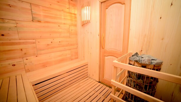 A wooden sauna room with benches, a door, and a stone-filled container. - samta (Tsqaltubo)