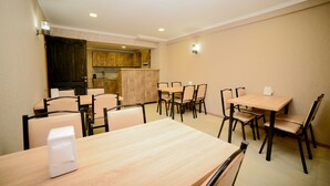 A dining area with wooden tables and chairs, a kitchen in the background, and a light fixture on the ceiling. - samta (Tsqaltubo)