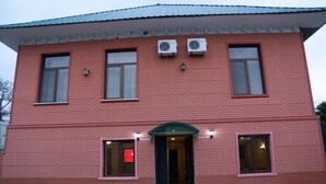 A red brick building with two air conditioning units, a green door, and two windows with lights. - samta (Tsqaltubo)