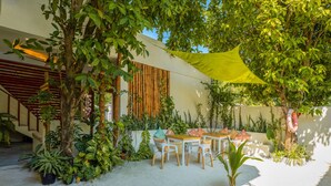 Un espace extérieur aménagé, abrité et doté de tables et de chaises, entouré de différents arbustes et arbres en pot.