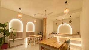 Un espace repas moderne avec une table et des chaises en bois, des luminaires suspendus et un ventilateur de plafond.