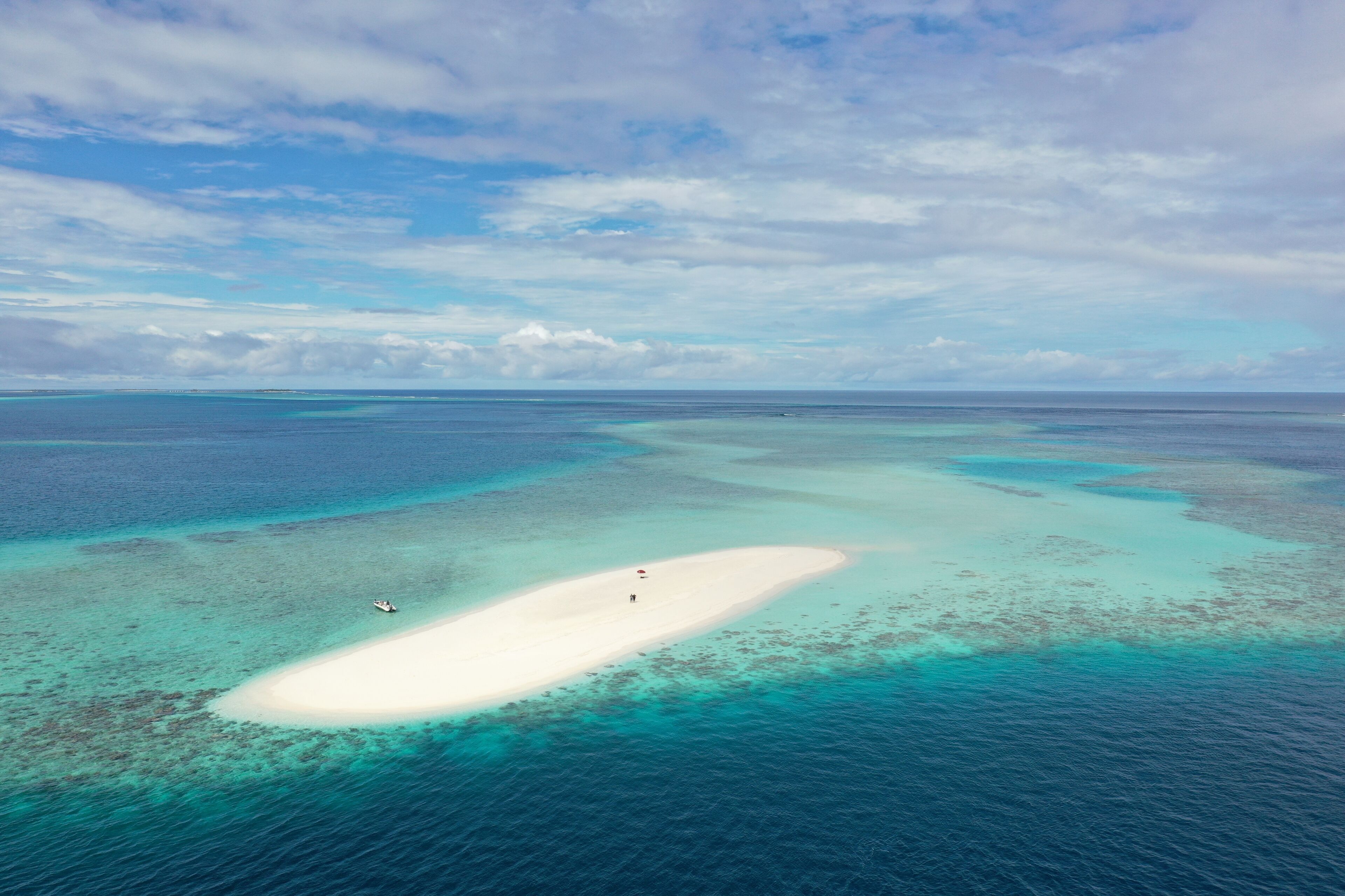 Vue aérienne d’une plage de sable blanc bordée d’eaux turquoise et de récifs coralliens.