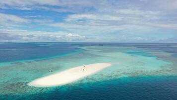 Vue aérienne d’une plage de sable blanc bordée d’eaux turquoise et de récifs coralliens.