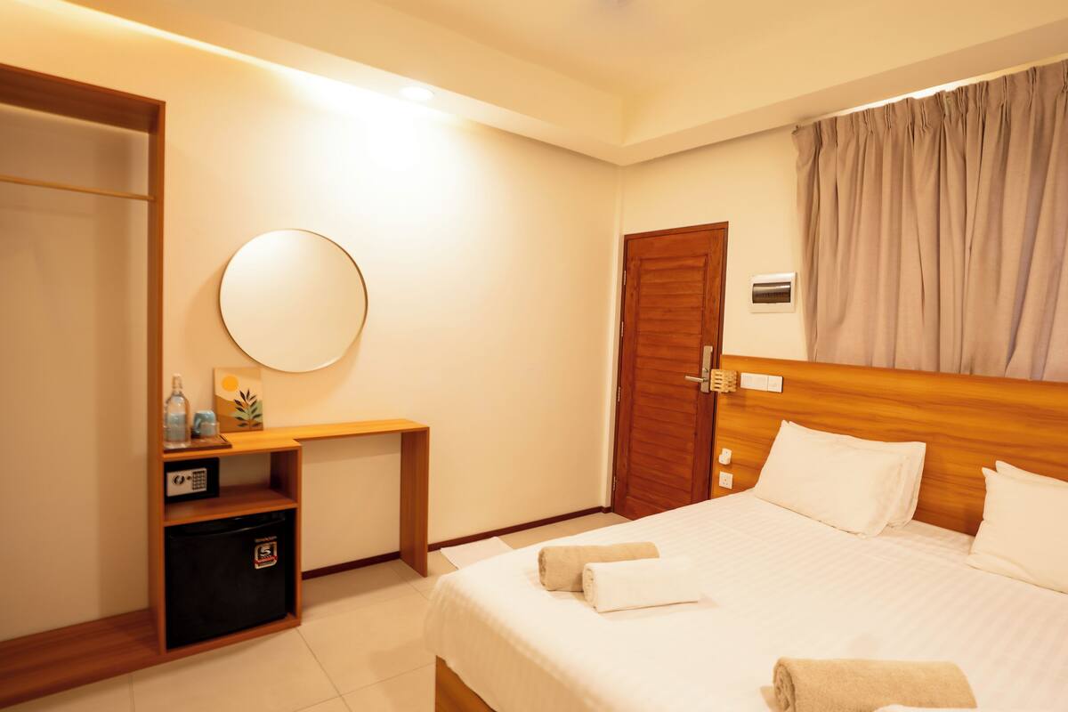 A hotel room with a bed, a desk with a computer, a wardrobe, and a mirror.