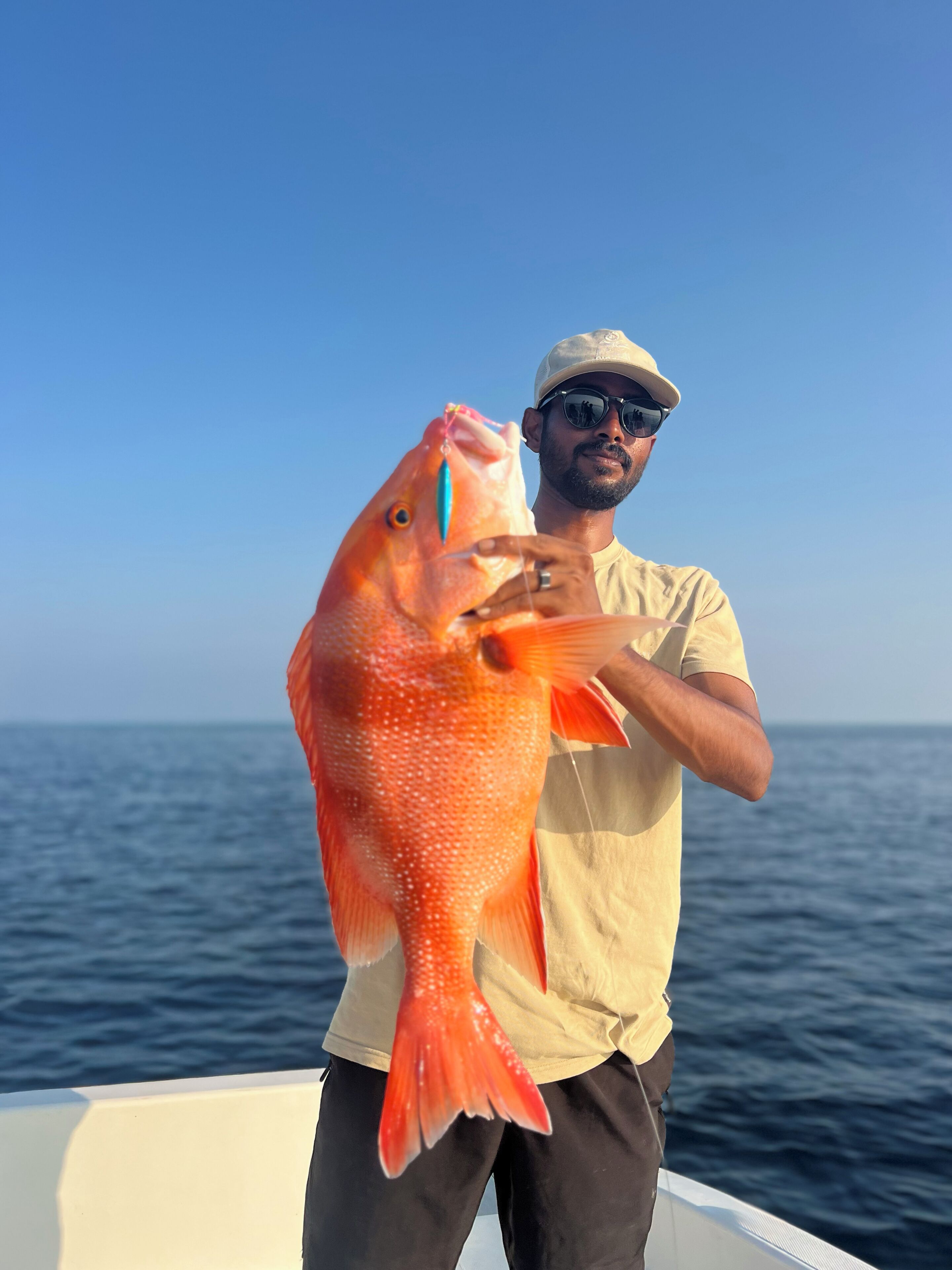 A person holding a fish on a boat with a clear sky in the background.