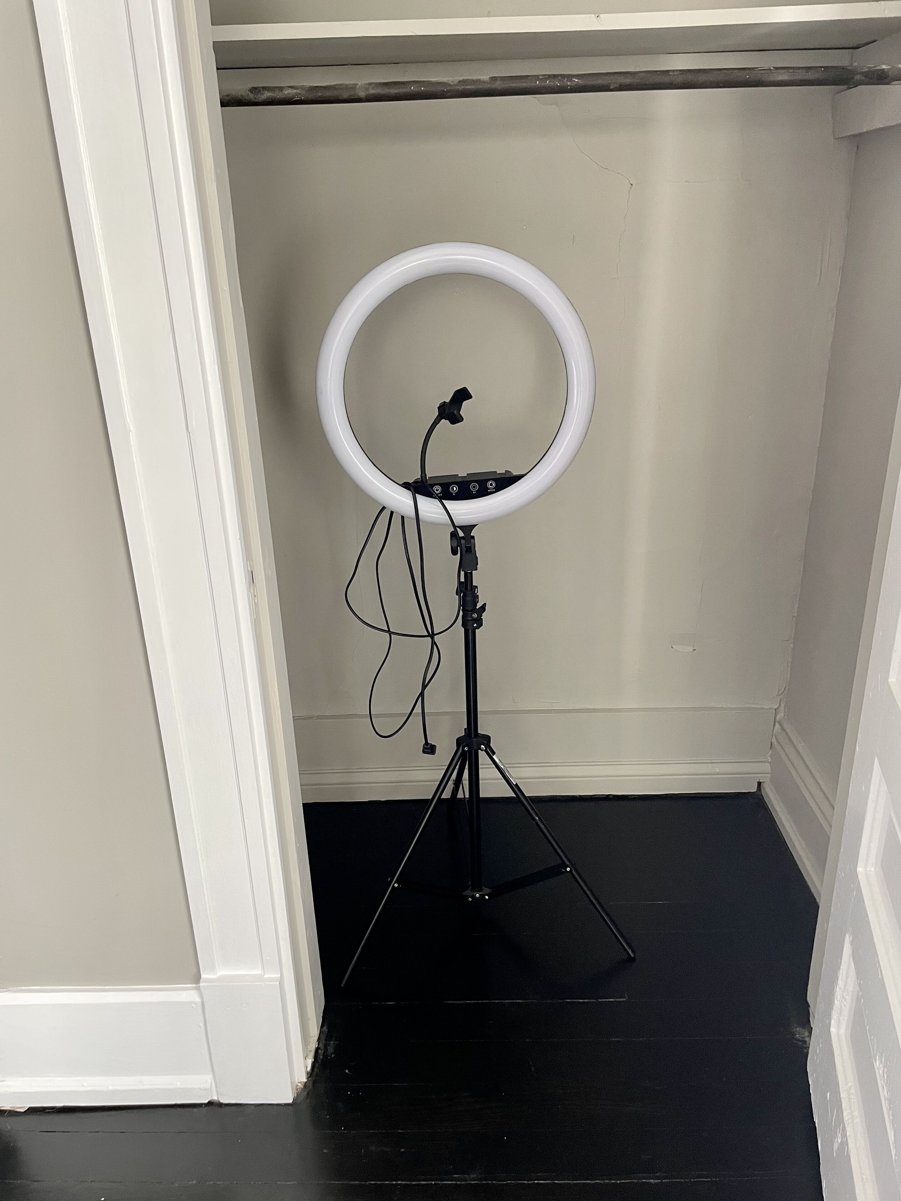 A ring light on a tripod stand in a room with a black floor and white walls.