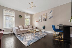 Un salon avec un canapé beige, une table basse en verre, un tapis bleu et blanc, un bar noir agrémenté de touches dorées et un lustre moderne.