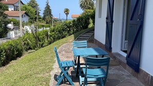 Eine Terrasse mit Tisch und Stühlen, ein Kiesweg und ein weißes Gebäude mit blauen Fensterläden.