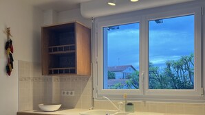 Eine Küche mit Holzausstattung, einem weißen Geschirrspüler und einem Fenster mit Blick auf Häuser und Bäume.