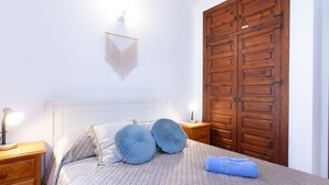A neatly made bed with a quilted bedspread and two pillows, a wooden nightstand with a lamp, and a wooden wardrobe with a handle. - Las Golondrinas by Interhome (Nerja)
