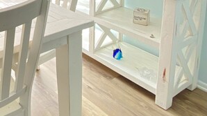 A dining area with a white table and chairs, a white console table with a sign, and three sunset paintings on the wall. - Charming Family Friendly Townhome Walk to Beach, Near AC Fun, Pet Friendly (Brigantine)