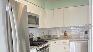 A modern kitchen with white cabinets, stainless steel appliances, a microwave, stove, oven, dishwasher, and a wooden floor. - Charming Family Friendly Townhome Walk to Beach, Near AC Fun, Pet Friendly (Brigantine)