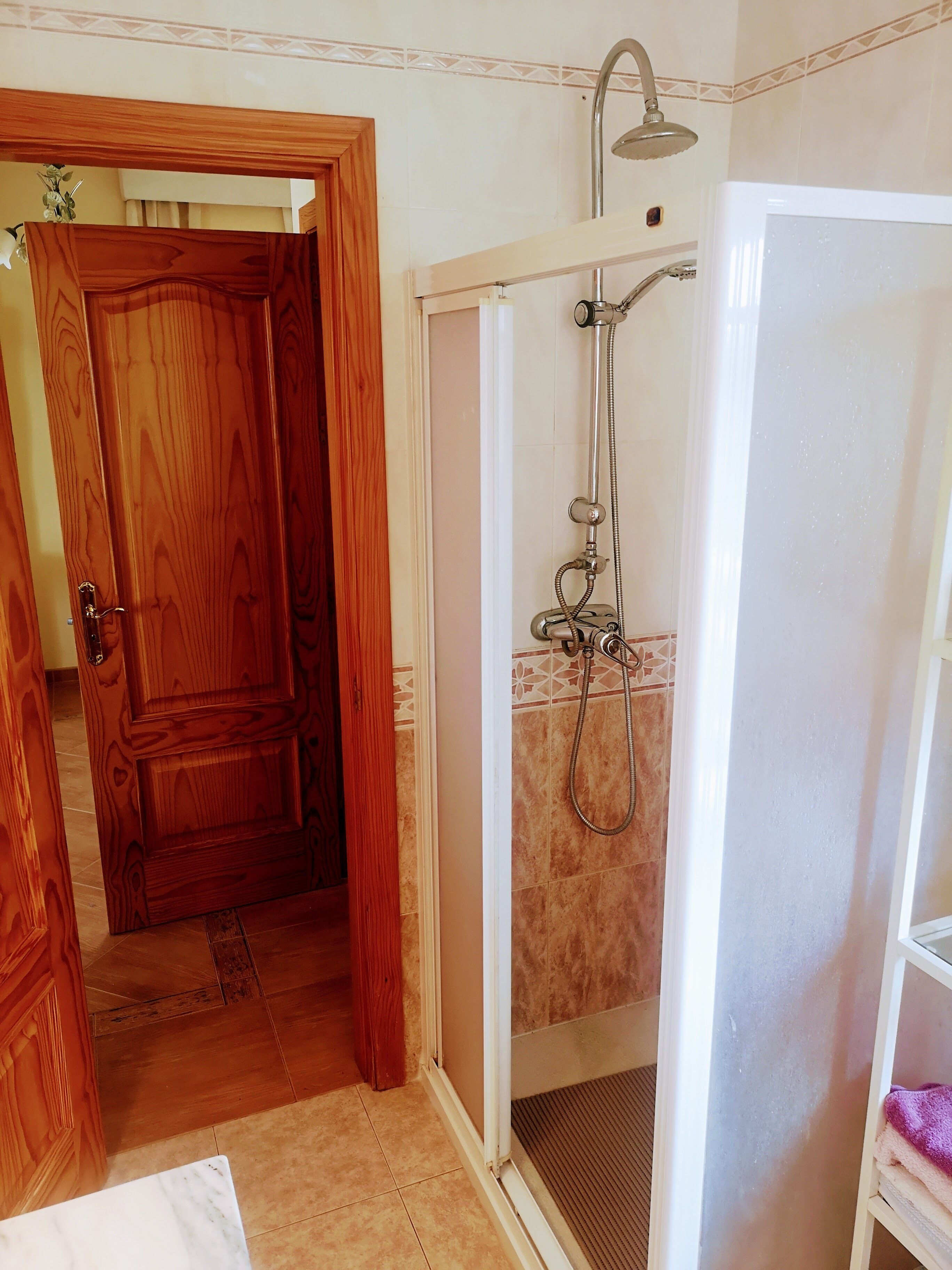 A bathroom with a shower, wooden door, and tiled floor.