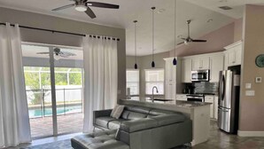 A modern living room with a gray sectional sofa, a kitchen with white cabinets, and a pool view. - Salt Water Pool & Spa Escape (North Port)
