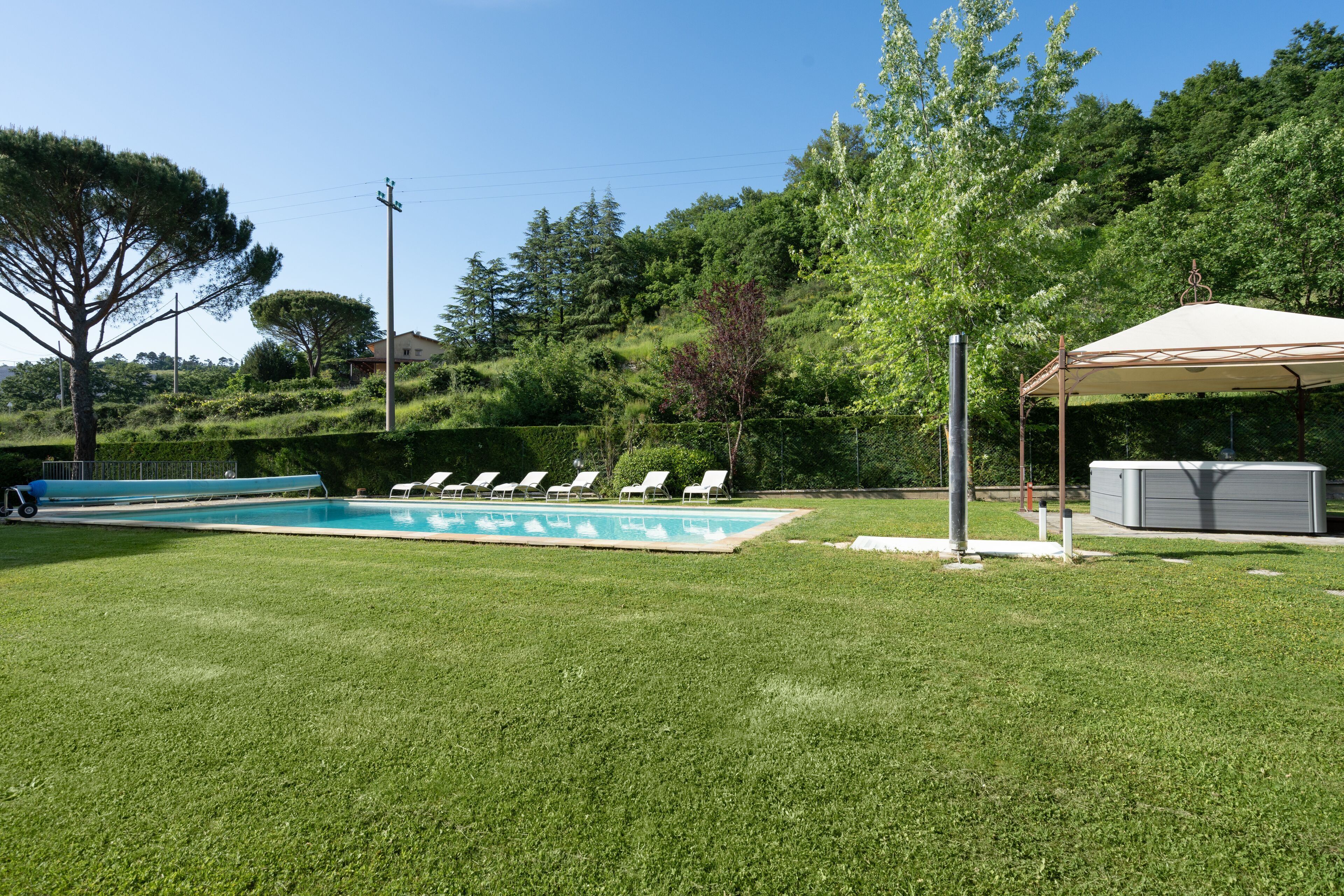 A backyard with a swimming pool, lounge chairs, and a covered area.